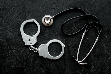 Medical lawsuit. Arrest for medical crime concept. Handcuff near stethoscope on black background...