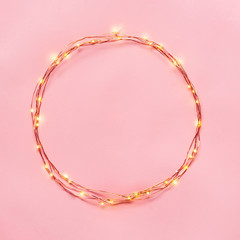 Christmas lights garland circular border over pink background. Flat lay, copy space.