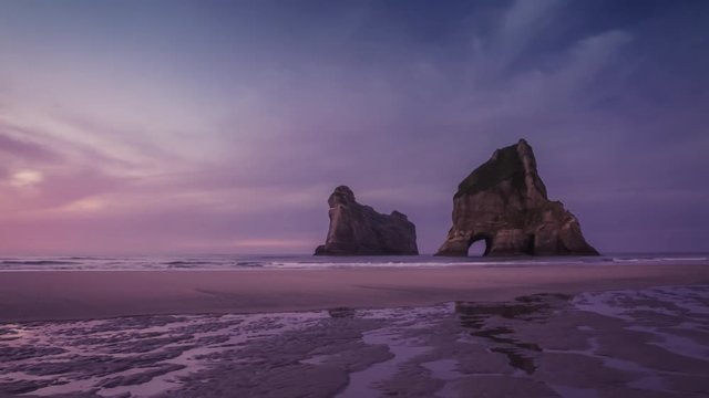 Spectacular empty beach with natural archway in rocks off the coast in beautiful colors of romantic evening. Wharariki Beach, New Zealand. Timelapse video.