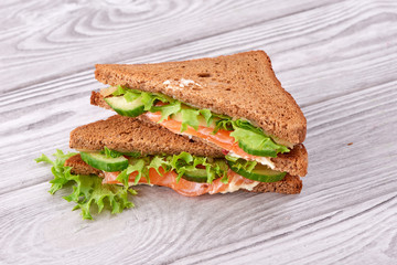 Sandwich with bread toasts, red fish salmon, fresh green leaves of salad and sliced cucumber