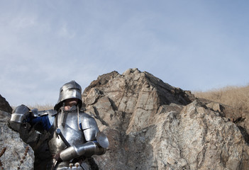 Fototapeta na wymiar Knight with a sword and in medieval armor on the background of granite stone