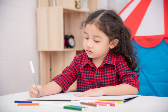 Little asian girl drawing picture by color marker on table at home