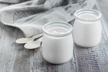 Greek yogurt in a glass jars with wooden spoons on wooden background. Healhty Breakfast Food. Copy space - 232912111