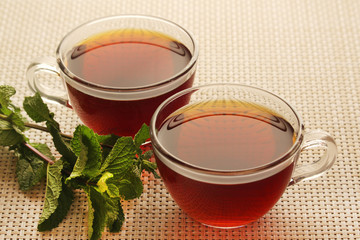 Two cups with black tea with fresh leaves of mint	