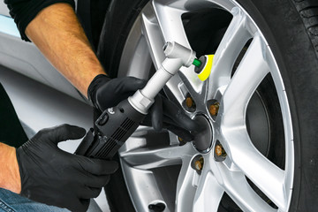 Car polish wax worker hands polishing car wheel. Buffing and polishing car disk. Car detailing. Man holds a polisher in the hand and polishes the car. Tools for polishing