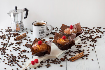 Three muffins, coffee mug, cinnamon, coffee pot, coffee beans on a white table