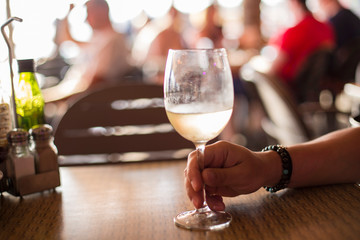 man's hand holding a glass of white wine in a bar