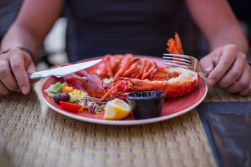 on the table in the plate lobster and grilled vegetables and the hands of men with cutlery in the restaurant