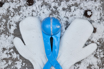 white mittens with tongs for snow balls on the background of snow-covered wooden surface with cones and snowflakes