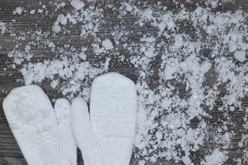 white mittens on the background of snow-covered wood surfaces with pine cones and snowflakes