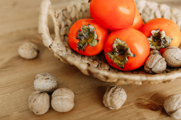 Persimmon fruits and walnuts in a wicker basket. Agriculture and harvesting concept