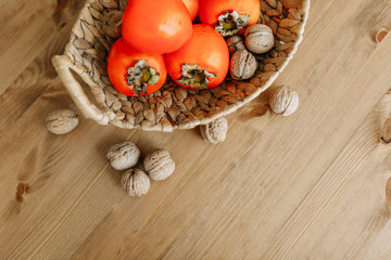 Persimmon fruits and walnuts in a wicker basket. Agriculture and harvesting concept