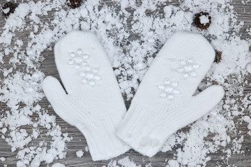 white mittens on the background of snow-covered wood surfaces with pine cones and snowflakes