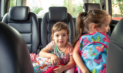 Children in the car go to school, happy, sweet faces of sisters