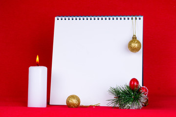 empty notebook with christmas decorations and burning candle on red background