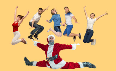 Freedom in moving. Mid-air shot of pretty happy young man and women jumping and gesturing against studio background. Runnin girl and Santa. Christmas and holiday concept