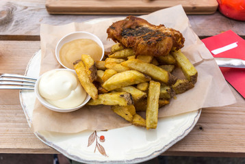 Fish and chips served with curry and tartar sauce on a plate with a paper. It is a hot dish of English origin consisting of fried battered fish and hot potato chips.