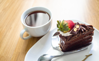 Black coffee In white glass with soft chocolate cake and dried flowers on the wood floor.