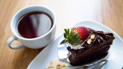 Black coffee In white glass with soft chocolate cake and dried flowers on the wood floor.