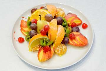 Sweet fresh fruits on white plate. Orange, apple, grapes, pear, kiwi, cherry. Healthy food style