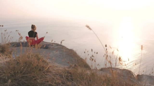 Beautiful view of woman doing yoga Baddha Konasana Bound Angle Pose on the mountain with sea view at sunset. Back view.