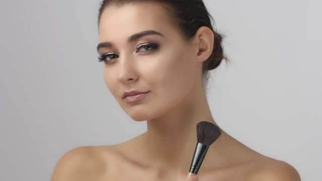 Beauty woman applying makeup. Beautiful girl applying cosmetic with a big brush. Gorgeous model gets blush on the cheekbones. Powder, rouge. Slow motion video footage in 4k UHD