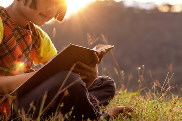 Obraz premium Cute little girl sitting on the grass and reading the book at sunset