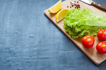 Fresh green lettuce, cherry tomatoes, lemon and spices on a wooden Board. dark background