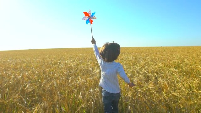 Cute cheerful boy holding toy wind turbine in hand, running at sunset. Wheat field. Happy kid, child playing, having fun wiht pinwheel. Happiness, nature, vacation, childhood, children, happy family