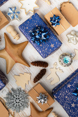 Fototapeta na wymiar Creative chritmas composition. Presents in dark blue wrapping paper with silver stars and sparkles, wooden decorations, ornaments, paper tags on white table, overhead view, selective focus