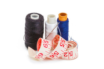 Needle, spools of thread, measuring tape and thimble as symbols for tailoring isolated on white...