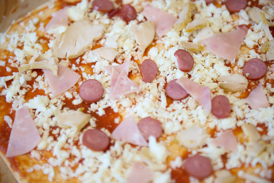 A close view of raw pizza, with tomato, cheese and bacon, before being cooked in an oven.