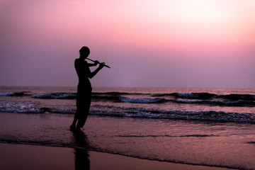 A man is practicing playing the flute on the birch in the sunset. GOA, India. 16.01.2018 © grthirteen