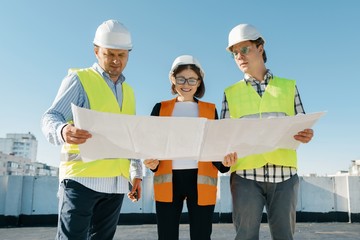 Team of builders engineers at a construction site, reading blueprint. Construction, development, teamwork and people concept