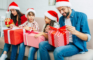 Big happy and cheerful family in santa hats giving christmas presents in living room while New Year holidays