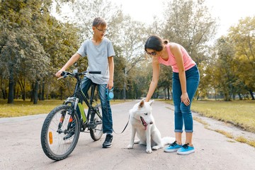 Obraz premium Children teenagers on the road in the park with white dog Husky with bike talking, smiling