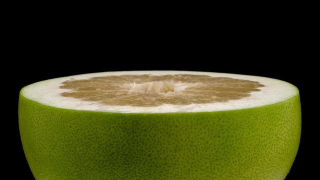 One half of big shaddock pomelo fruit. Rotating on the turn table. Isolated on the black background. Close-up. Macro.