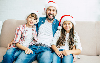 Handsome father with him son and daughter. Happy young family in red santa hats spending time together at home while winter holidays