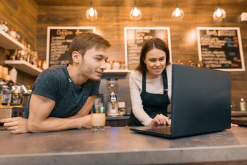 Young couple man and woman owners of small modern coffee house using laptop computer for work