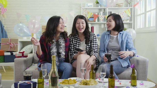 slow motion of young girls pointing finger to tv watching comedy at house party. group of best friends relax chilling eating drinking at home on weekend holidays. happy friendship meet up concept.