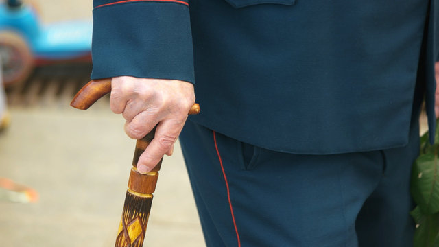 Old military man with a walking cane. Close up hand of an elderly War veteran using walking stick outdoors. Day of Victory.