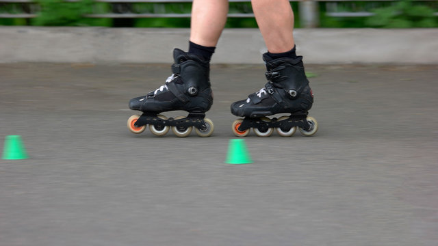 Boy riding on rollers in the summer park. Legs of boy on rollers, cropped image. Kid learning to roller skate on the road with cones.