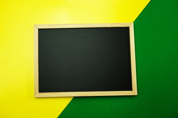 empty blackboard on yellow and green background flat lay