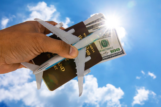 thailand passport - travelling by air - dollar money with aircraft modell in the dand against blue sky