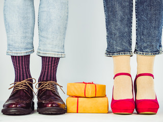 Male and female legs in stylish shoes, two gifts in a yellow wrap and red ribbons on a white isolated background. Concept of style, fashion, beauty
