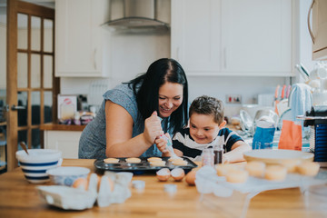 Mother helping son to put frosting onto cupcakes