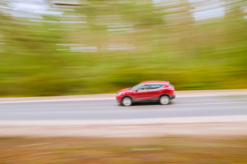 Fototapeta premium Szybko poruszający się czerwony samochód na drodze asfaltowej. Panoramowanie, rozmyte tło.
