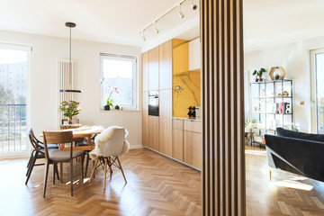 Stylish scandinavian open space with dining and living room with design sofa and family table. Bright and sunny room with big windows and brown wooden parquet.	 - obrazy, fototapety, plakaty