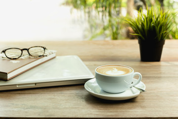 Coffee cup with laptop computer and glasses on wooden table.