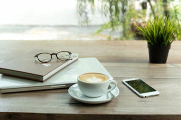 Coffee cup and cell phone and laptop computer with glasses on wooden table.